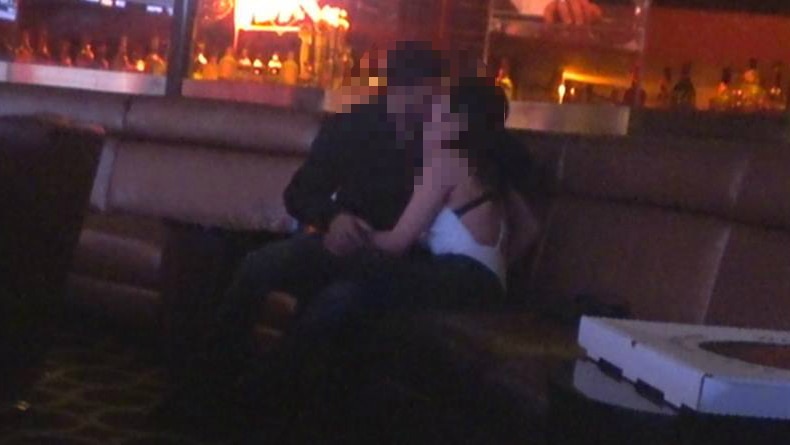A man and woman, shot from a far, kiss in a nightclub.