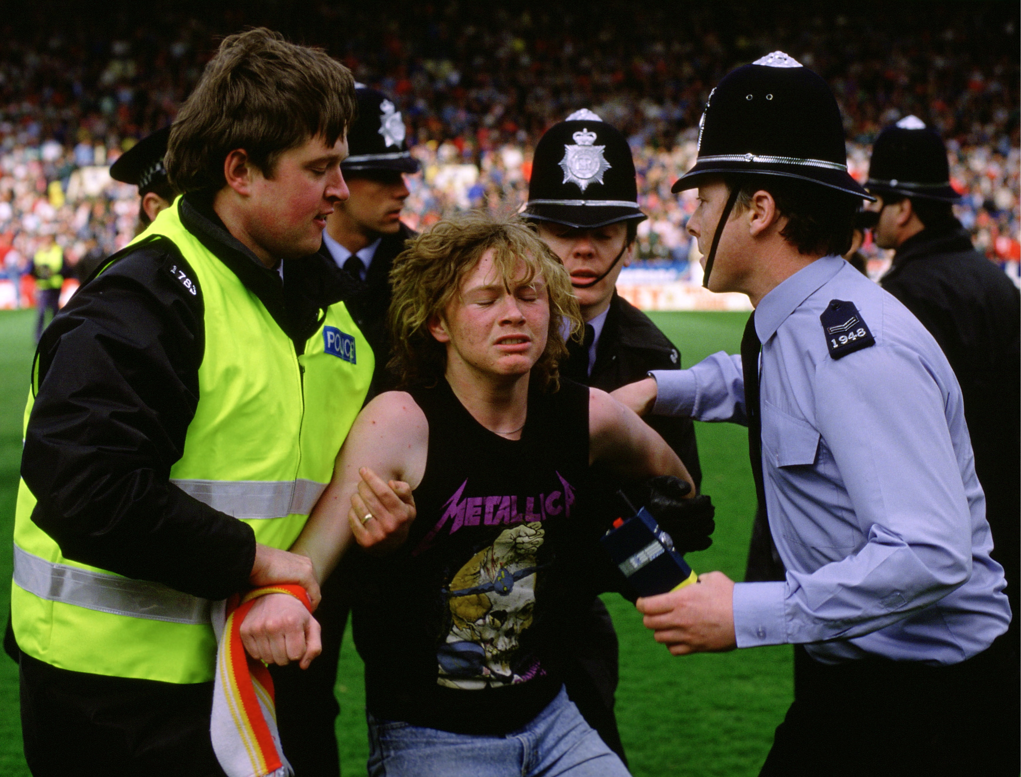 A man held up by police on a football pitch. 