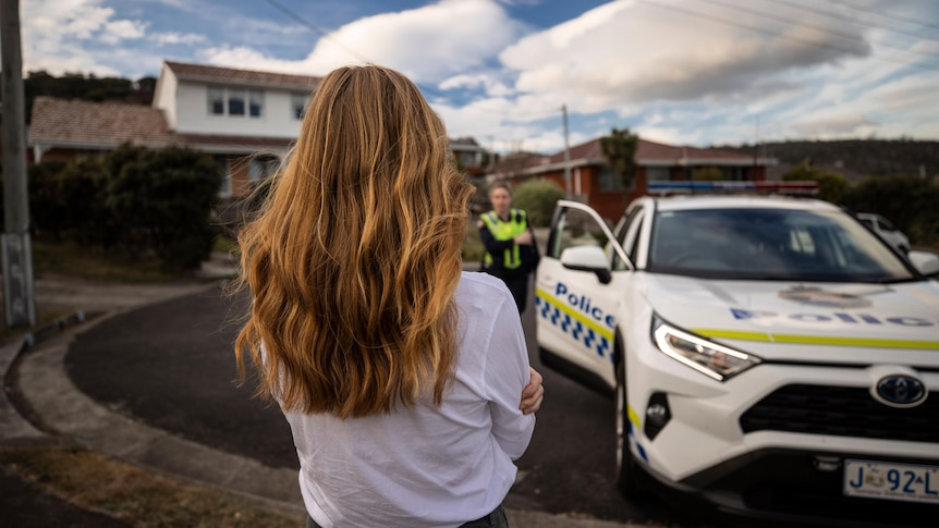 An unidentified woman watches as police approach from a police car.