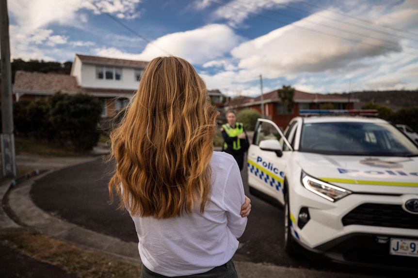An unidentified woman watches as police approach from a police car.