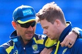 Justin Langer puts his arms around Steve Smith, who is looking down with his eyes closed, both wearing blue training kit