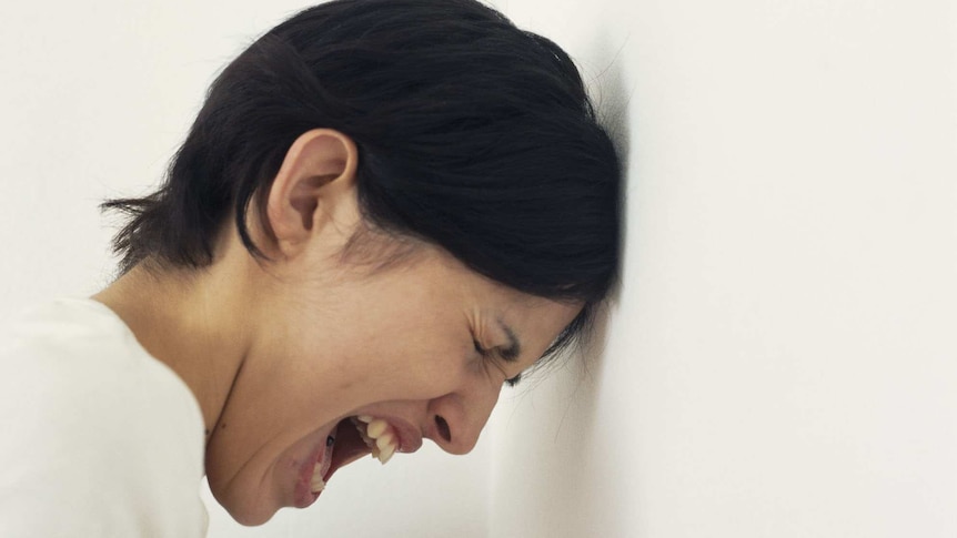 Woman with leaning her had against a wall screaming.