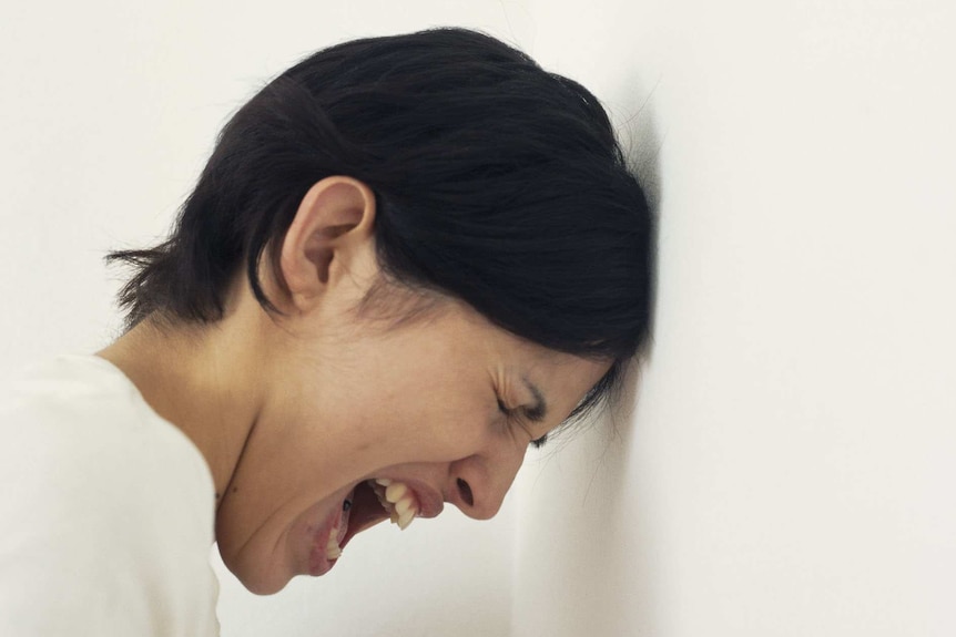 Woman with leaning her had against a wall screaming.
