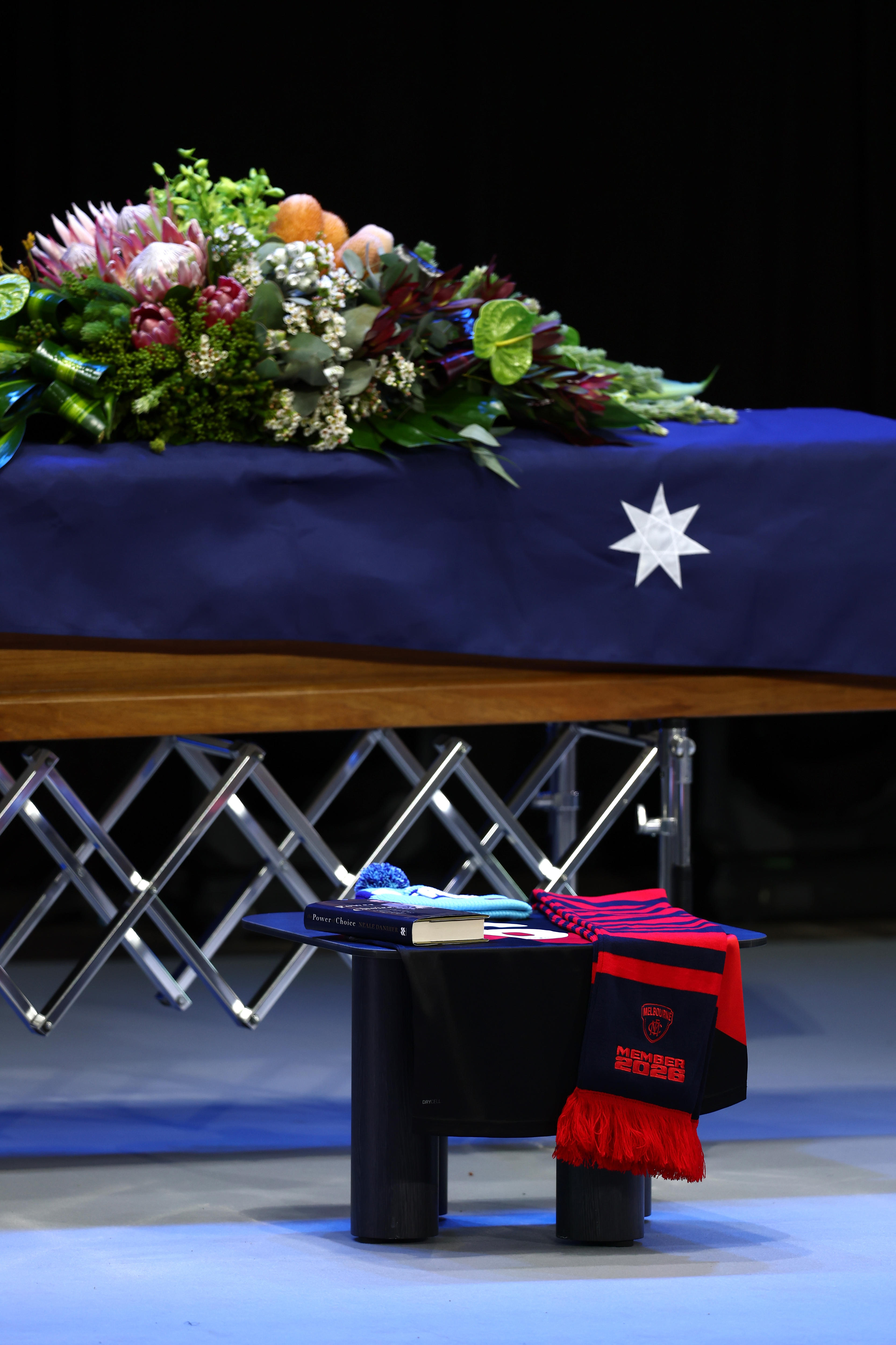 A blue beanie and a red and blue scarf lie beside a coffin draped in the Australian flag and native flowers.