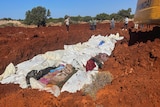 Bodies wrapped in blankets are placed into a mass grave, an excavator can be seen in upper right corner
