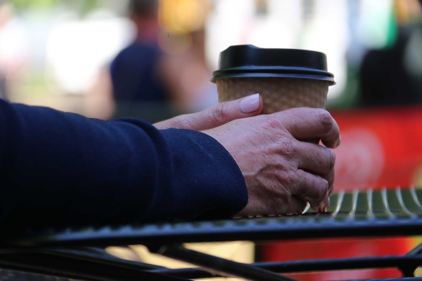 Hands holding a takeaway cup of coffee.