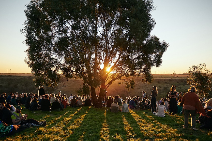 A crowd of people watch the sunset over a valley at Golden Plains