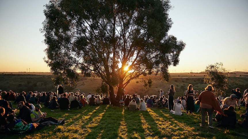 A crowd of people watch the sunset over a valley at Golden Plains