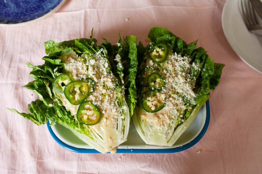 Two halves of a cos lettuce topped with Caesar salad dressing, sliced jalapenos and pecorino cheese, a quick salad to share.