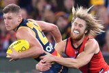 A male AFL player haolds the ball with his left hand as he is tackled around the waist by an opposition player.