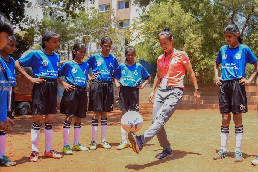 Bala Devi holds a soccer ball on her foot while girls watch on.