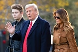 Barron, Donald and Melania Trump walk across a vedant lawn during autumn on the grounds of the White House.