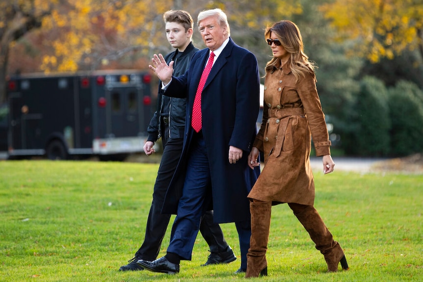 Barron, Donald and Melania Trump walk across a vedant lawn during autumn on the grounds of the White House.
