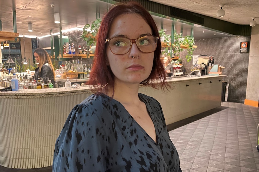 Teddy Sweeney has red hair and a nose ring and looks sideways while sitting at a bar.