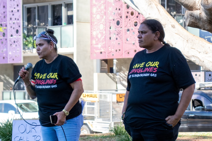 Two Indigenous women in dark shirts speaking at a community rally.