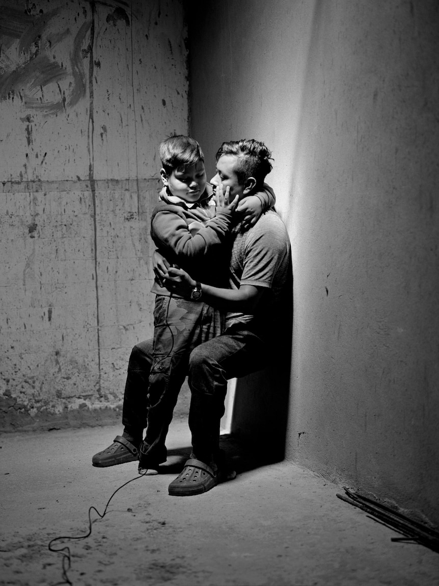 A father and son hug, in a concrete room.