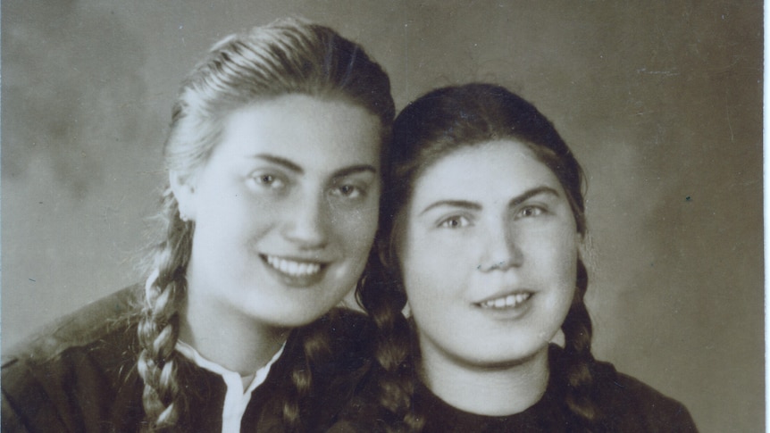 A black and white portrait of two young women smiling at the camera with long plaited hair.