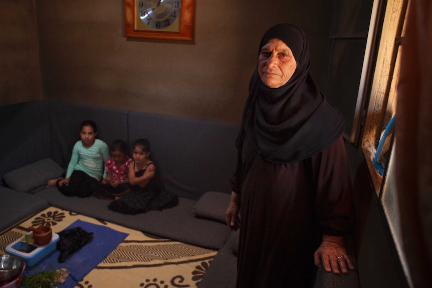Zouhair Amar wears black ands stares at the camera as her grandchildren sit in the background