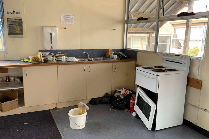 A kitchen with rubbish on the floor and a broken stove