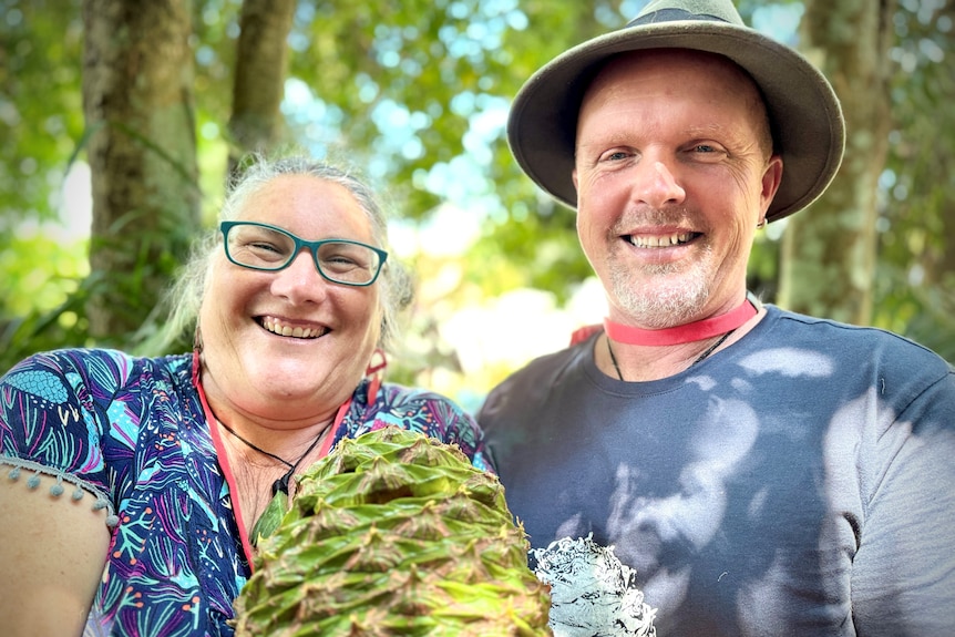 A woman and man pose with a large green Bunya Pine cone.