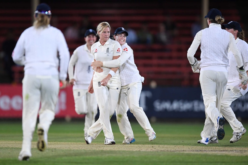 Katherine Brunt is standing, being hugged by a teammate after taking a wicket.