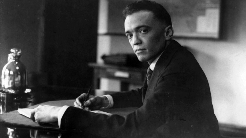 A black and white photo of J Edgar Hoover sitting at a writing desk.