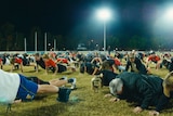 Scores of players, coaches and support staff at the Morningside AFL club in Brisbane doing push-ups on the field.