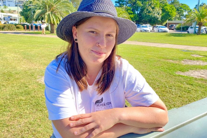 Woman sits at a picnic table, sunny day and gently smiling