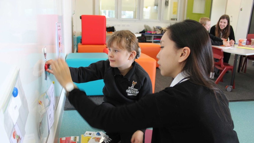 child and student sit and work at a white board