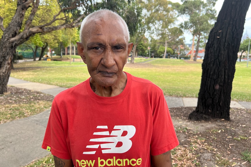 A headshot of a man with a solemn look on his face. He is in a public park