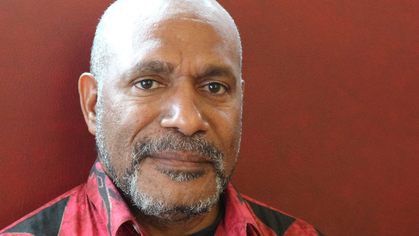 A portrait of Benny Wenda against a red backdrop.