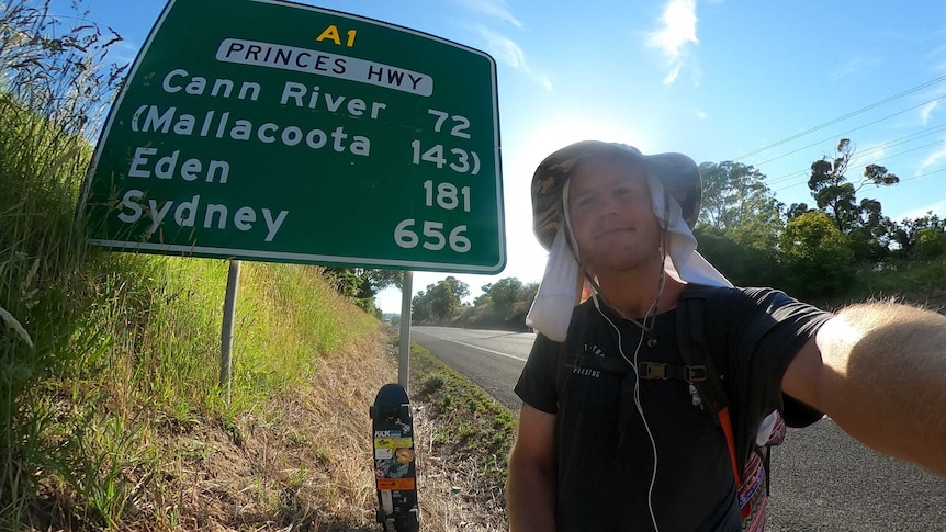 Tom Drury pictured with a sign showing half way through his 1200 kilometre month-long skate from Melbourne to Sydney.