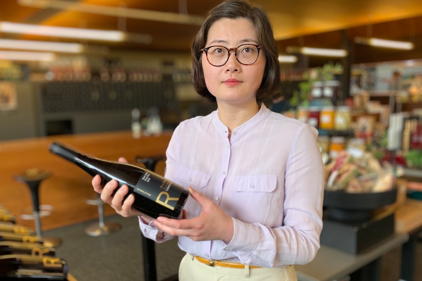 A woman holds a wine bottle at a cellar. 