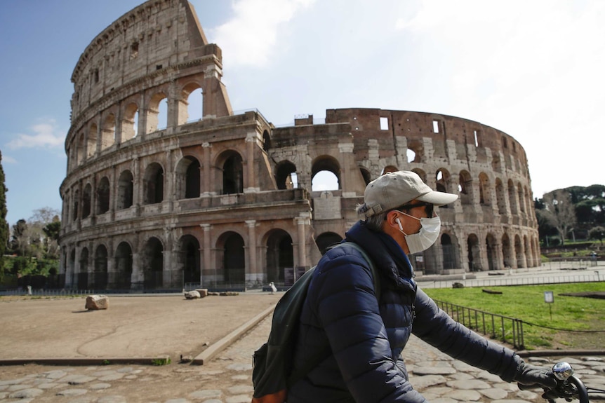 A man wearing a mask rides past an empty Colosseum in Rome