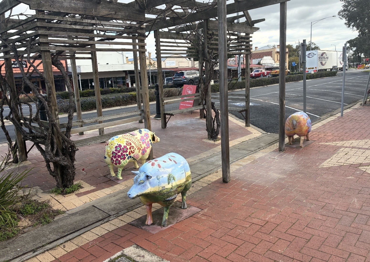 Three sheep statues with brightly painted patterns and landscapes on them stand alongside Kaniva's main street.