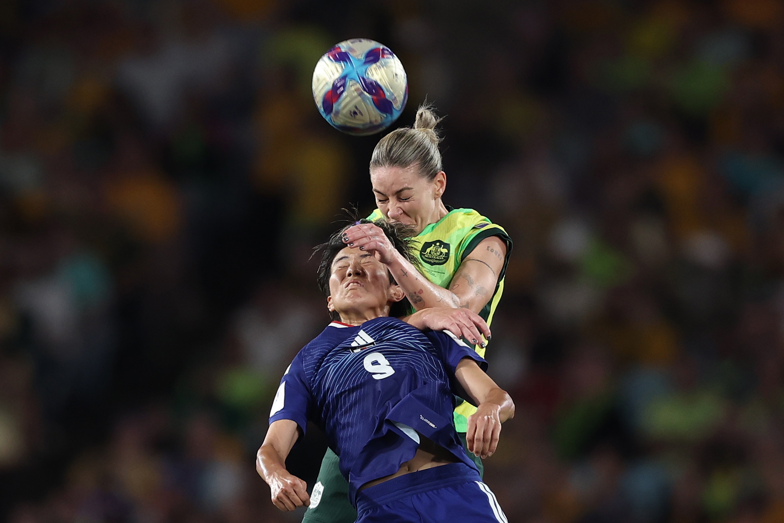 Un futbolista vestido de amarillo se levanta para cabecear el balón y salta sobre un jugador vestido de azul.