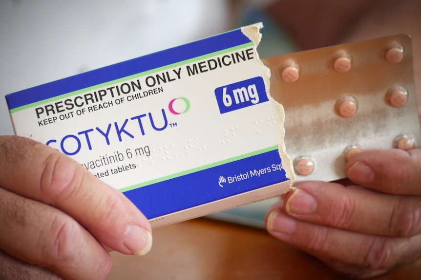 Hands holding a box of medication labelled 'Sotyktu' and blister pack of pills