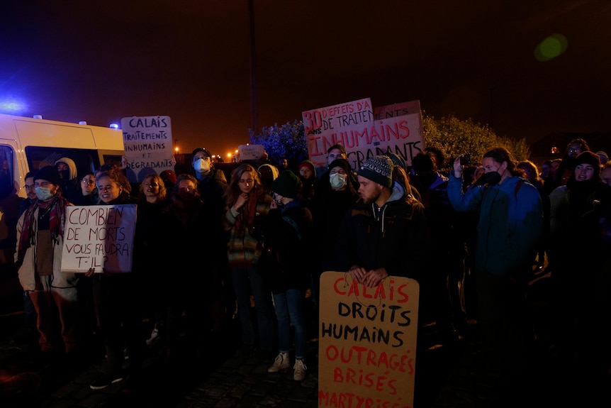 Protesters holding placards in French at night. 
