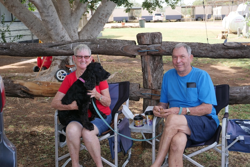An older couple sit outside with a small black dog.