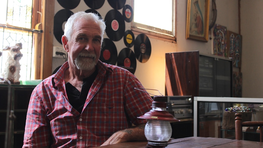 Warren Smith sitting at a wooden table with records and paintings in the background.