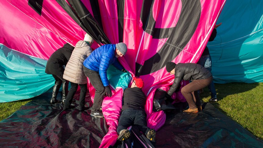 Pilot Chris Shorten lies his weight on the deflating balloon as passengers help him wrangle the collapsing fabric.
