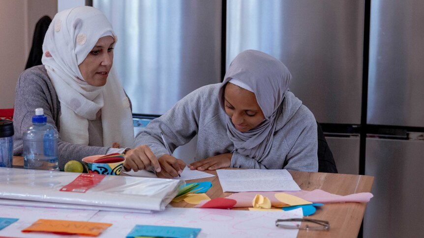 A mother instructs her daughter as she writes.