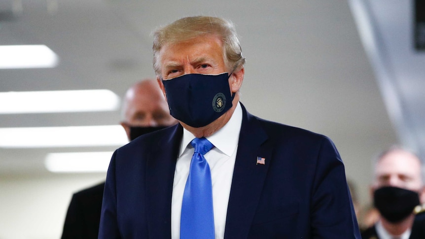 President Donald Trump wears a black face mask as he walks down a hallway.