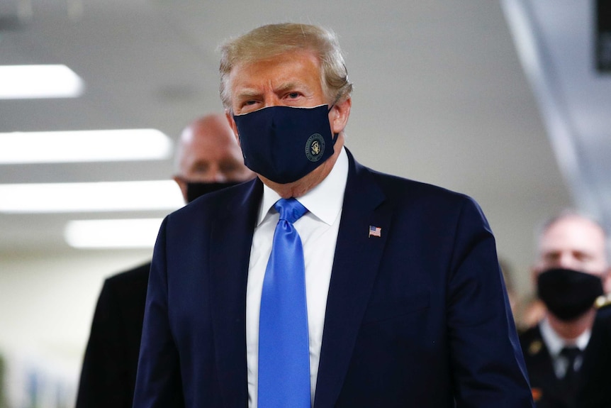 President Donald Trump wears a black face mask as he walks down a hallway.