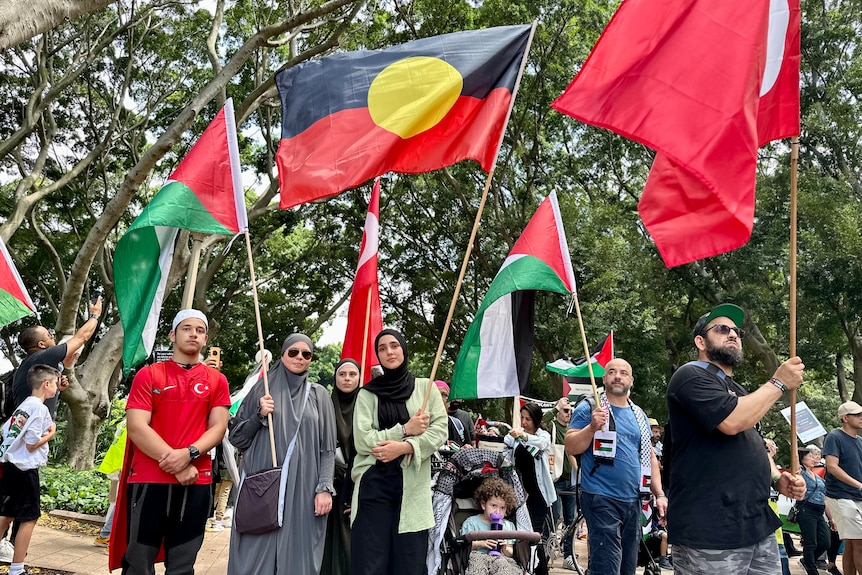 Palestinian people stand at a protest holding an Aboriginal Flag and a Palestinian flag