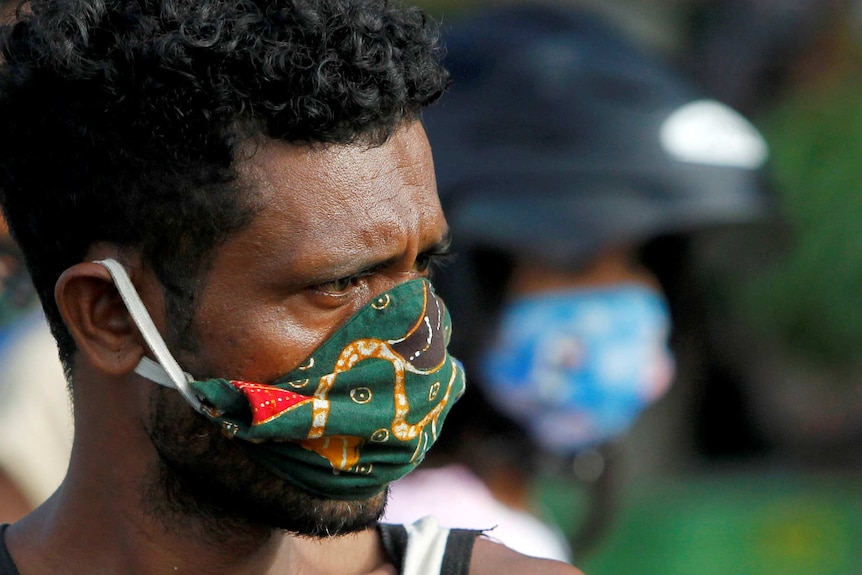 A vendor wearing a protective mask looks on as he waits for customers