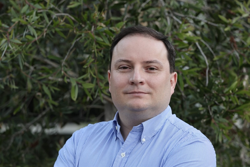 A man in a collared shirt looks at the camera.