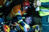 Mine workers wearing high-vis clothing attending to injured worker underground in dark with head lamp turned on.