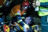 Mine workers wearing high-vis clothing attending to injured worker underground in dark with head lamp turned on.