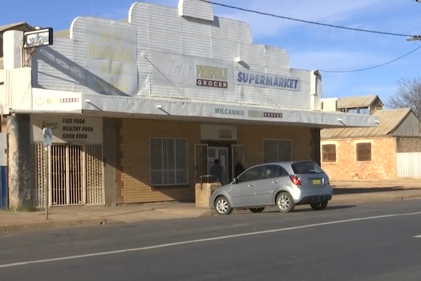 A supermarket in Wilcannia with a white car parked out the front of it. 